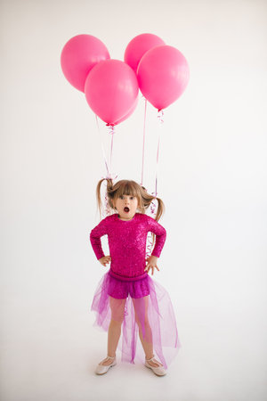 Cute happy child girl 4-5 year old wear princess dress posing with balloons having birthday party over white in room. Childhood.の写真素材