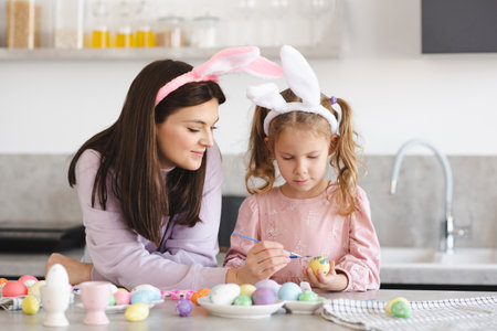 Young mother painting Eater eggs with her child girl daughter 4-5 year old at kitchen table together. holiday season celebration. springtime. motherhood.の写真素材