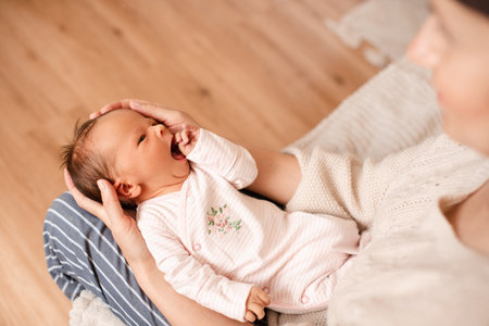 Mother holding crying infant baby girl with colic pain on hands wear pajamas in room at home top view. motherhood.の写真素材