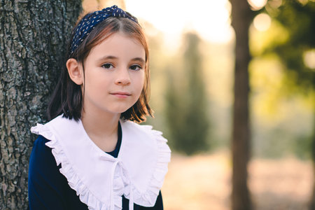 Cute child girl 6-7 year old wear school dress with white collar outdoor over nature background. looking at camera.の写真素材