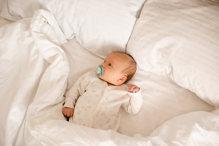 Cute little infant baby 1-2 months old wake up in bed lying on white duvet top view. Good morning. Childhood.の写真素材