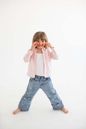 Cute funny child girl 4-5 year old wear casual clothes denim pants with shirt and un glasses posing over white in room. Childhood.の写真素材