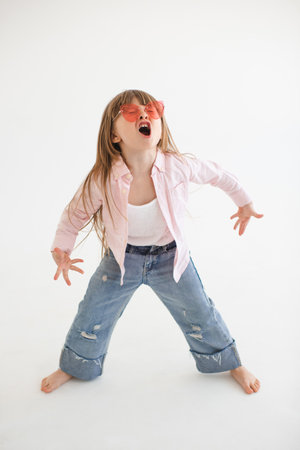 Funny child girl 4-5 year old wear casual clothes denim pants and shirt with sun glasses screaming or sing rocking over white indoor. Childhood.の写真素材