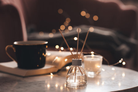 Glass bottle of home fragrance with bamboo sticks and scented candle stay on marble coffee table...