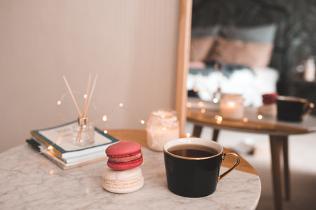 Cup of coffee with macarons and stack of paper books with candle on marble table in bedroom top view closeup.の写真素材