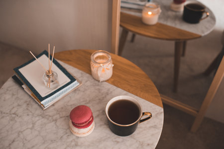 Cup of coffee with macarons and stack of paper books with candle on marble table in bedroom top view closeup.の写真素材