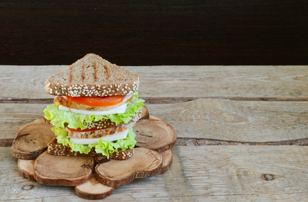 Sandwich of triangular bread with chicken breast tomato and cheese Wooden rustic backgroundの写真素材