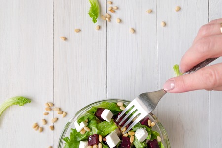 Salad of Beetroot, Feta cheese and lettuce leaves with pine nuts and fork in woman hand. Empty spaceの写真素材