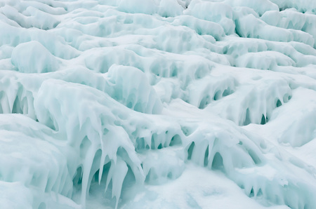 Ice splashes on frozen rocks and stones, formed during freezing of lake