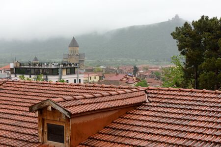 Tile roofs of central part of Mtskheta and view of Svetitskhoveli Cathedral on foggy rainy morning