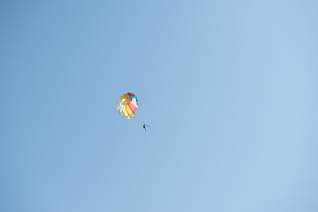 Man flying on a parachute behind a boat on a background of clear blue skyの写真素材