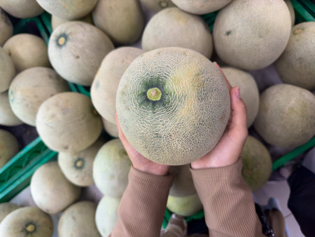 Person Holding Fresh Melon in Grocery Store Produce Sectionの写真素材