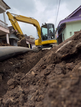 Excavator Digging Trench in Urban Residential Street Constructionの写真素材