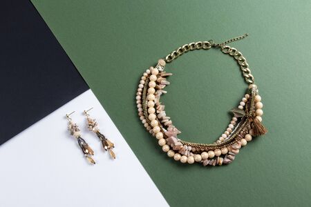 set of earrings and multi layer pearl necklace with stones and gold plated chain boho style on green and black paper backgroundの写真素材