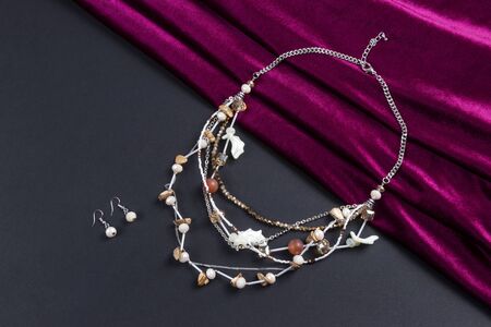 set of earrings and multi layer crystal beads necklace with stones and sea shell silver chain boho style on red satin scarf and black paper backgroundの写真素材