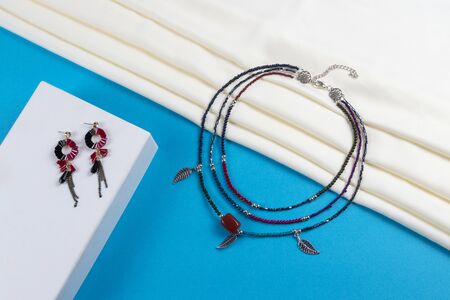 set of tassel earrings and necklace made of colorful seed beads and metal feathers boho style on white scarf and blue paper backgroundの写真素材