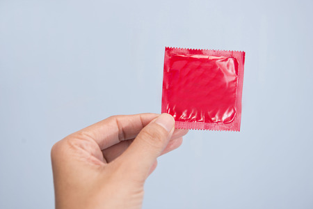 Hand holding condom in red plastic bagの写真素材