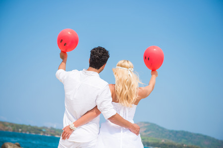 bride and groom holding red balloon on the beach, honeymoonの写真素材