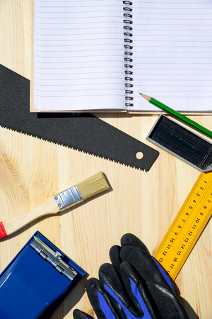Workplace and tools of a carpenter or builder.Hand saw, ruler, brush, notebook, pencil, sandpaper, and work glovesの写真素材