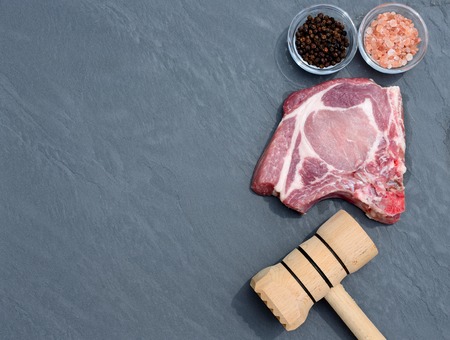Pork steak and wooden hammer on the table top in natural stoneの写真素材
