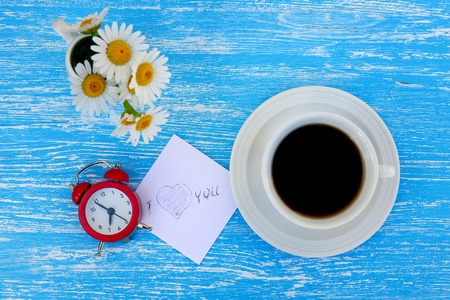 Daisy flowers, alarm clock and cup of coffee with I love you note on rustic blue wooden backgroundの写真素材