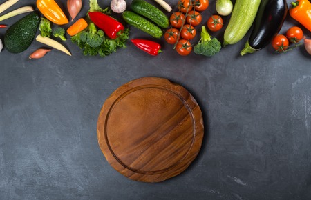 Empty wooden round cutting board and different vegetables on a black background for displaying productsの写真素材