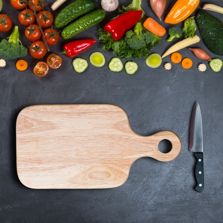 Vegetables, empty wooden cutting board and chef's knife on a black background for displaying productsの写真素材