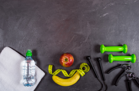Fitness background. Dumbbell, apple, banana, water bottle, towel,skipping rope,measuring tape on grey background. Top viewの写真素材