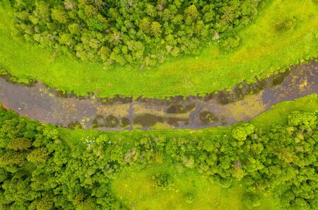 Aerial drone view of river overgrown with reeds and grass cutting trough forestの写真素材