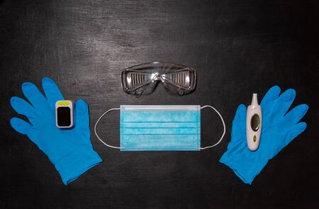 Black medical background. Safety goggles, medical mask, two blue gloves, thermometer and oximeterの写真素材