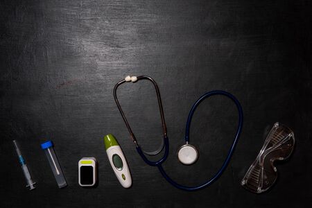 Stethoscope, thermometer, oximeter, syringe and test tube on a black background. Doctor's equipment for taking tests for infection with the virus Covid-19の写真素材