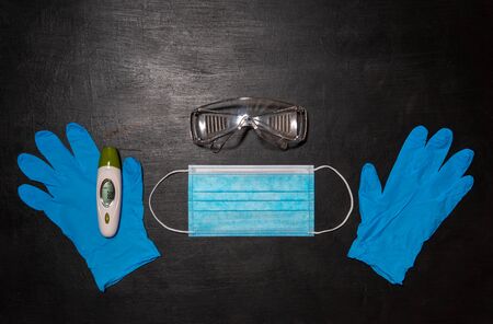 Safety goggles, medical mask, two blue gloves and thermometer. Black medical backgroundの写真素材