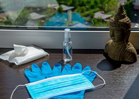 Medical gloves, mask, antiseptic gel, antibacterial wipes and Buddha head statue on the windowsillの写真素材