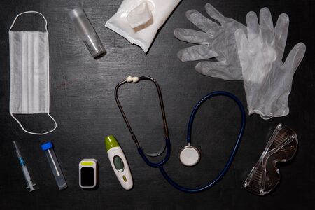 Doctor's equipment-stethoscope, thermometer, oximeter, test tube, medical mask, disposable gloves, antiseptic gel, antibacterial wipes and syringe on black backgroundの写真素材