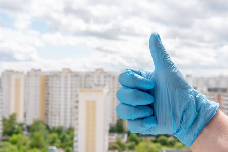 A male hand in a medical glove showing a finger up gesture against a cityscapeの写真素材