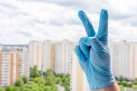 A male hand in a medical glove showing V sign for victory or peace gesture against a cityscapeの写真素材