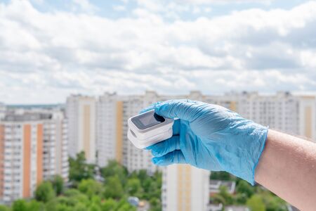 Male hand in medical glove holds oximeter on cityscapeの写真素材