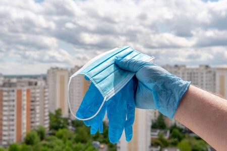Male hand in medical glove holds a protective mask and disposable gloves on cityscapeの写真素材