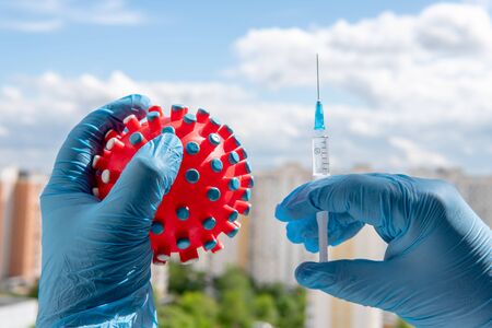 A male hand in a medical glove squeezes a symbolic virus. Second hand injects a virus vaccine. Victory in fight against Pandemic Covid-19の写真素材