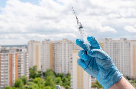 Male hand in medical glove holds syringe on cityscapeの写真素材