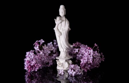 Guanyin framed by pink lilac flowers on a black background with reflectionの写真素材