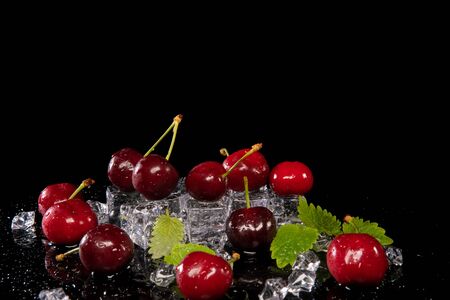 Cherries, mint leaves and ice cubes on a black background with reflectionの写真素材