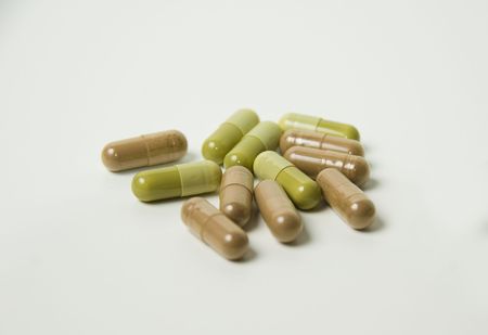 Brown and green capsules scattered on white background