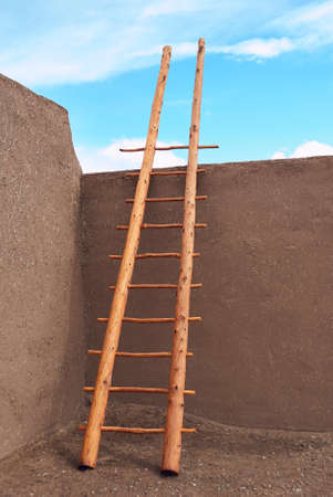 Wooden ladder leaning on wall pointing into blue skyの写真素材