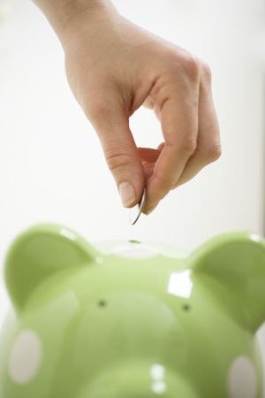 Hand placing coin in green piggy bank の写真素材