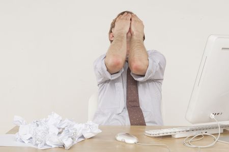 professional man sitting at desk with face in hands 