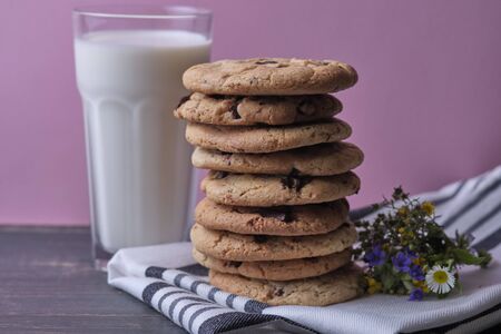 American chocolate cookies, a glass of milk and wild flowers. Dark wooden table and pink background.の写真素材