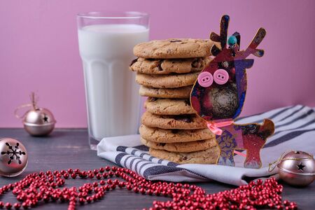 American chocolate cookies, a glass of milk and Christmas decorations. Dark wooden table and pink background. Cookies for the New Year.の写真素材