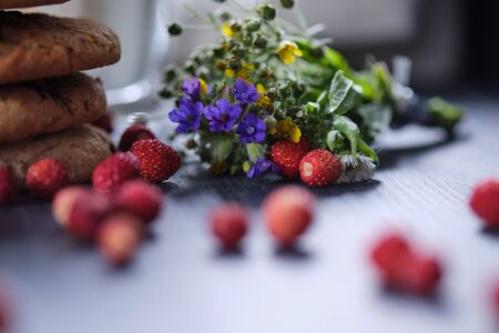 American chocolate chip cookies on a table and in a glass jar stacked on top of each other. Cookies, a glass of milk, strawberries, flowers and a linen towel. Rural still life.の写真素材