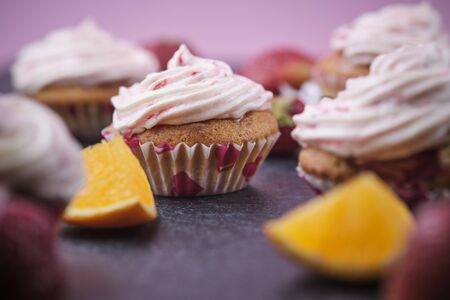 Orange cupcakes with strawberry filling and butter cream with fresh berries. Desserts on a dark background.の写真素材